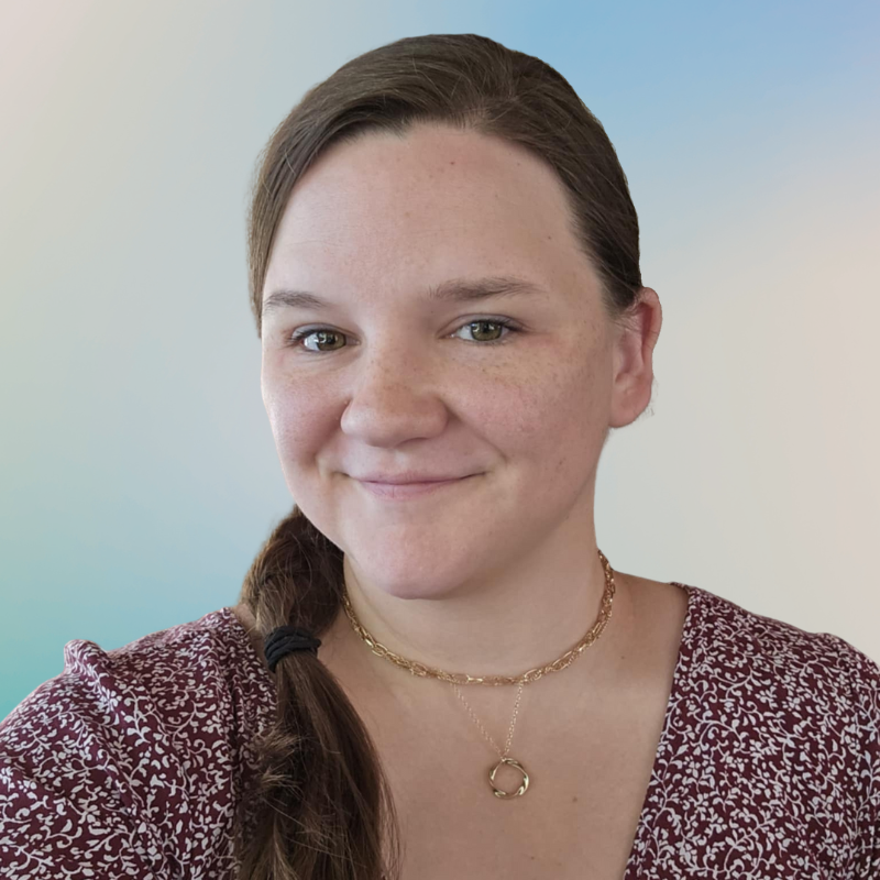 Headshot of a young woman with long braided hair, wearing a red patterned top and necklace.